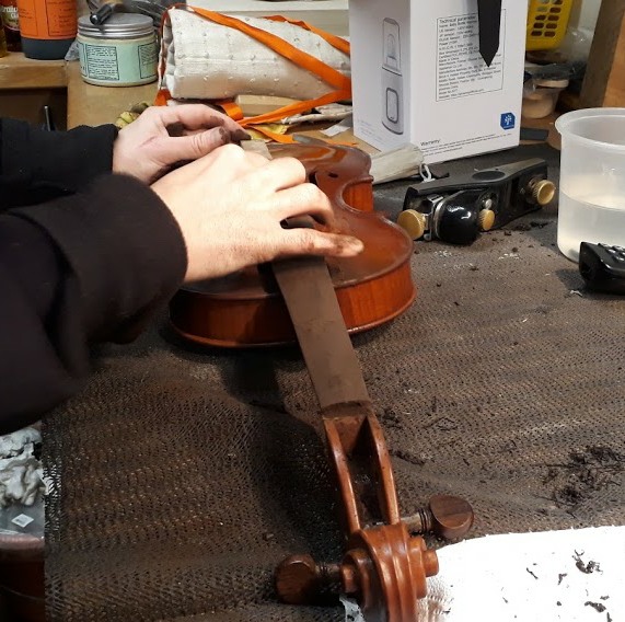 Violin on the bench having it's fingerboard being re-profiled